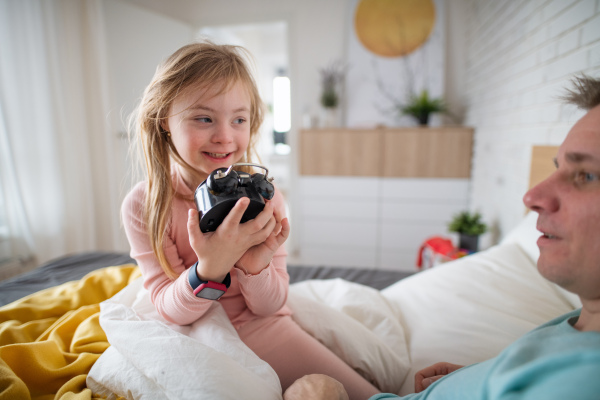 A father setting alarm clock with his little daughter with Down syndrome in bed at home.