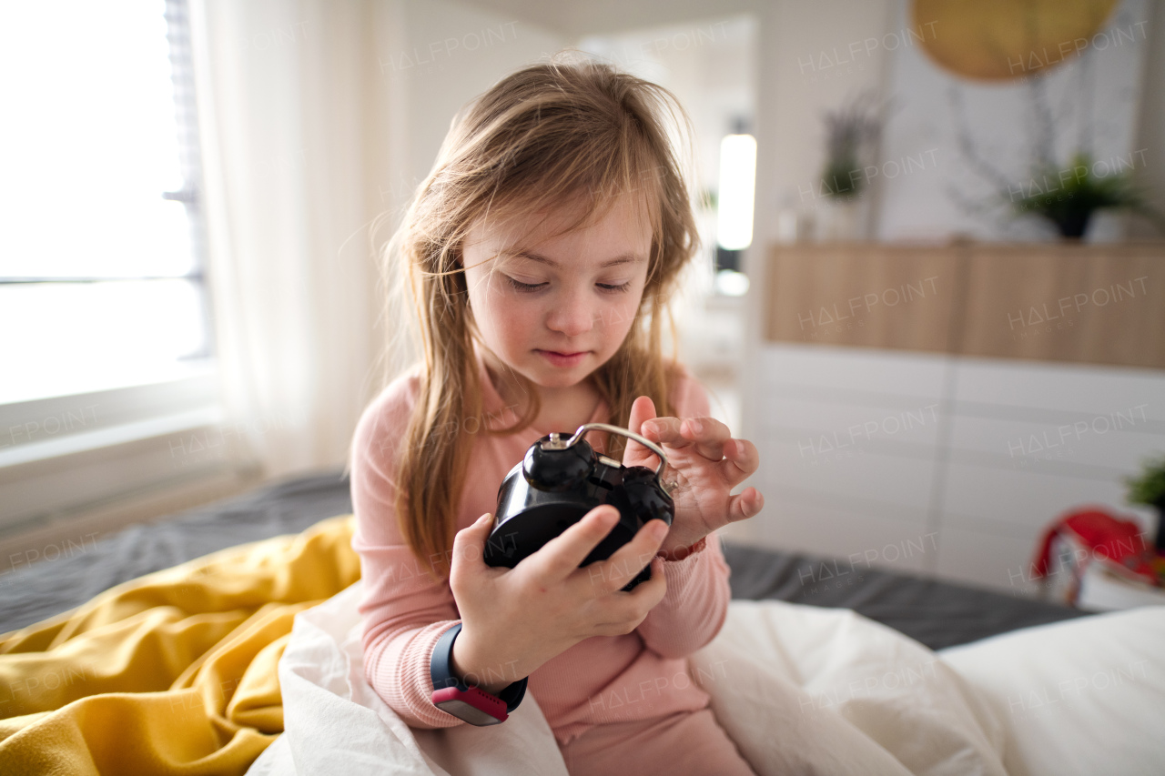 A little girl with Down syndrome playing with alarm clock at home.