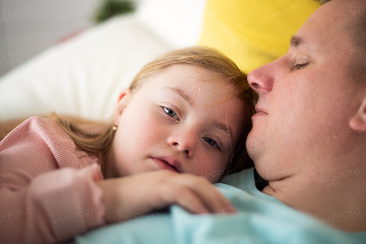 A father resting with his little daughter with Down syndrome in bed at home.