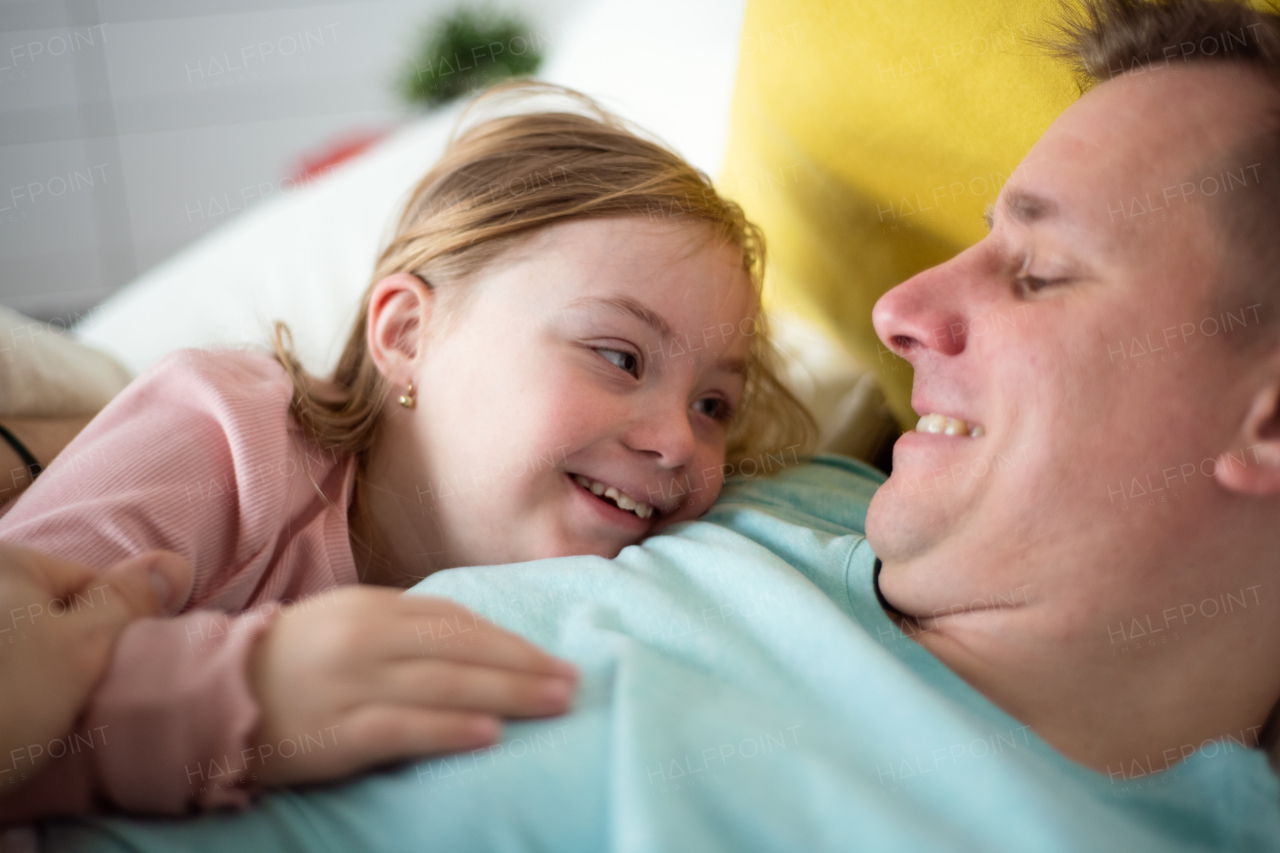 A father with hugging his little daughter with Down syndrome on bed at home.