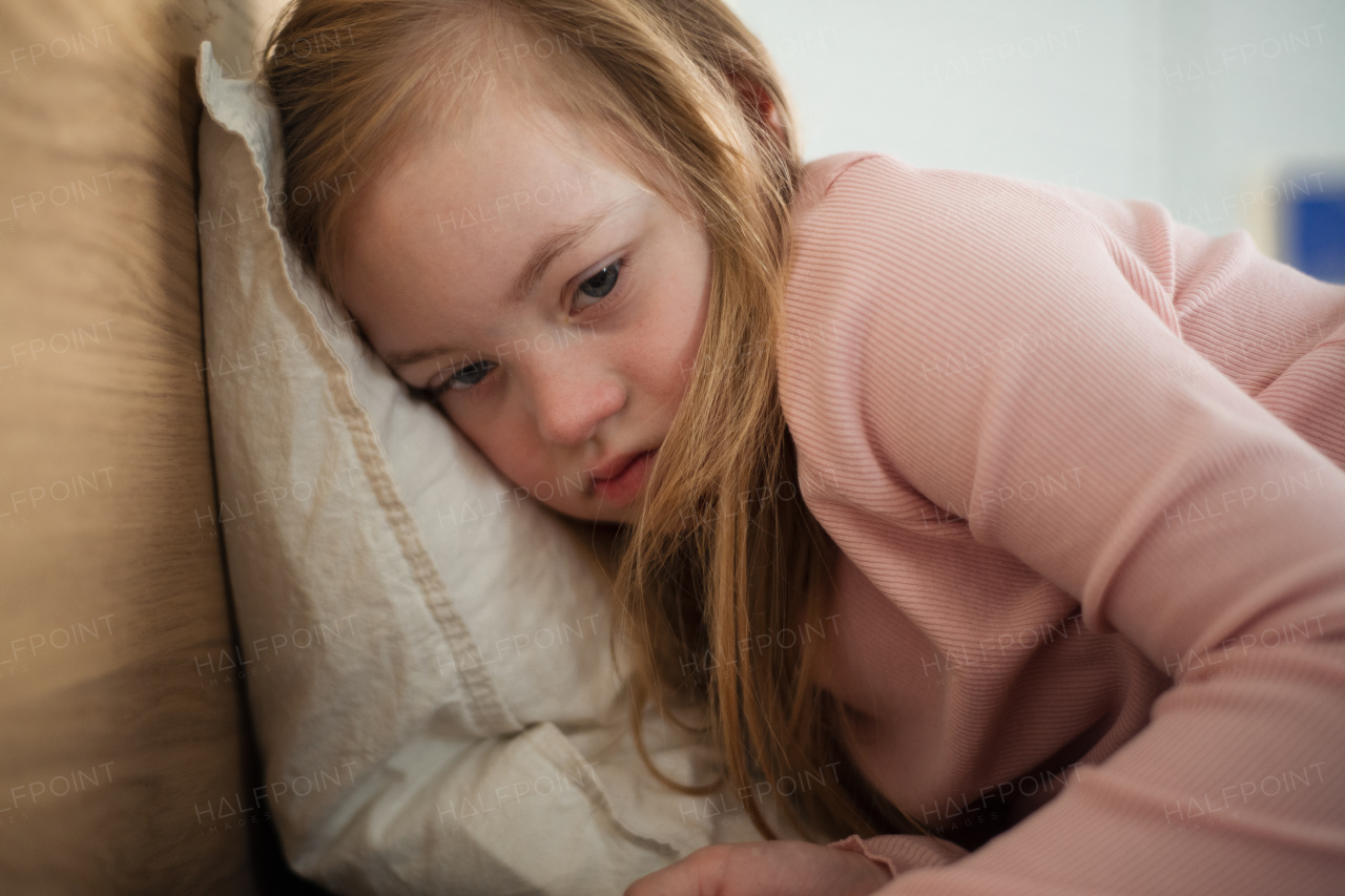 A sad little girl with Down syndrome lying on bed at home.