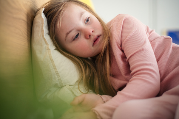 A sad little girl with Down syndrome lying on bed at home.