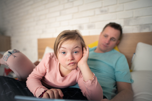 A father resting with his little daughter with Down syndrome in bed at home.