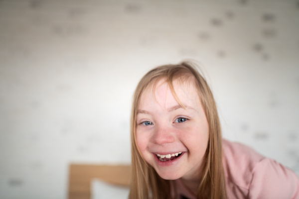 A happy little girl with Down syndrome looking at camera at home.