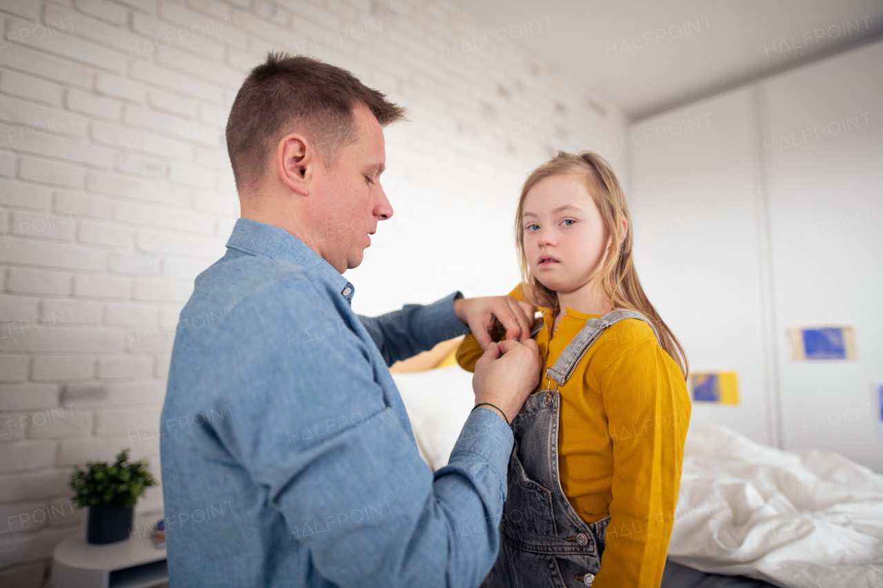 A father putting on different socks to his little daughter with Down syndrome when sitting on bed at home.