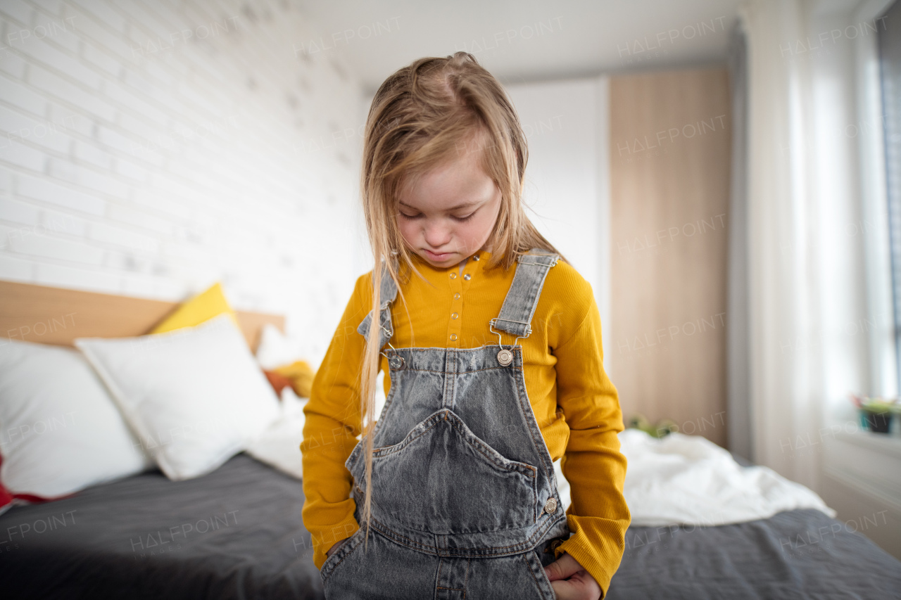 A sad little girl with Down syndrome looking down at home.