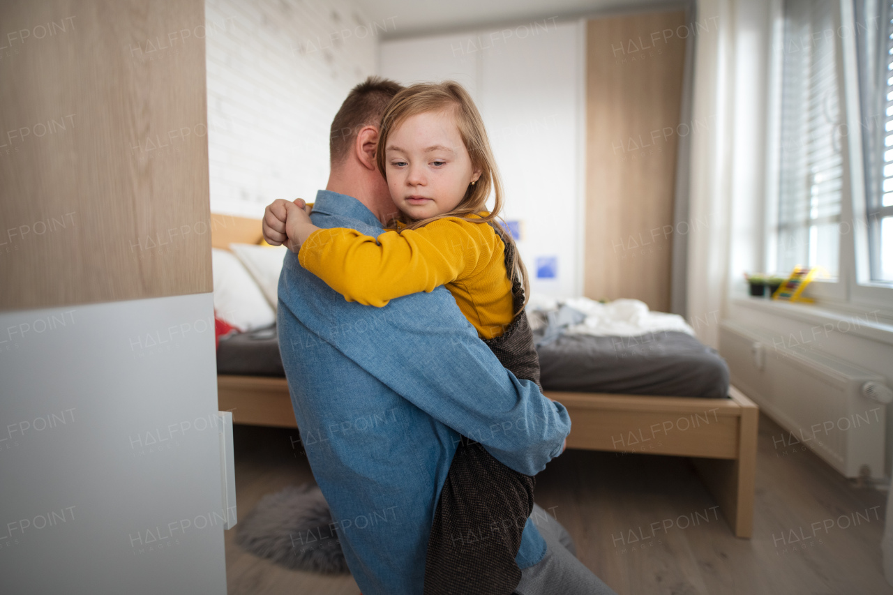 A father hugging his little daughter with Down syndrome at home.