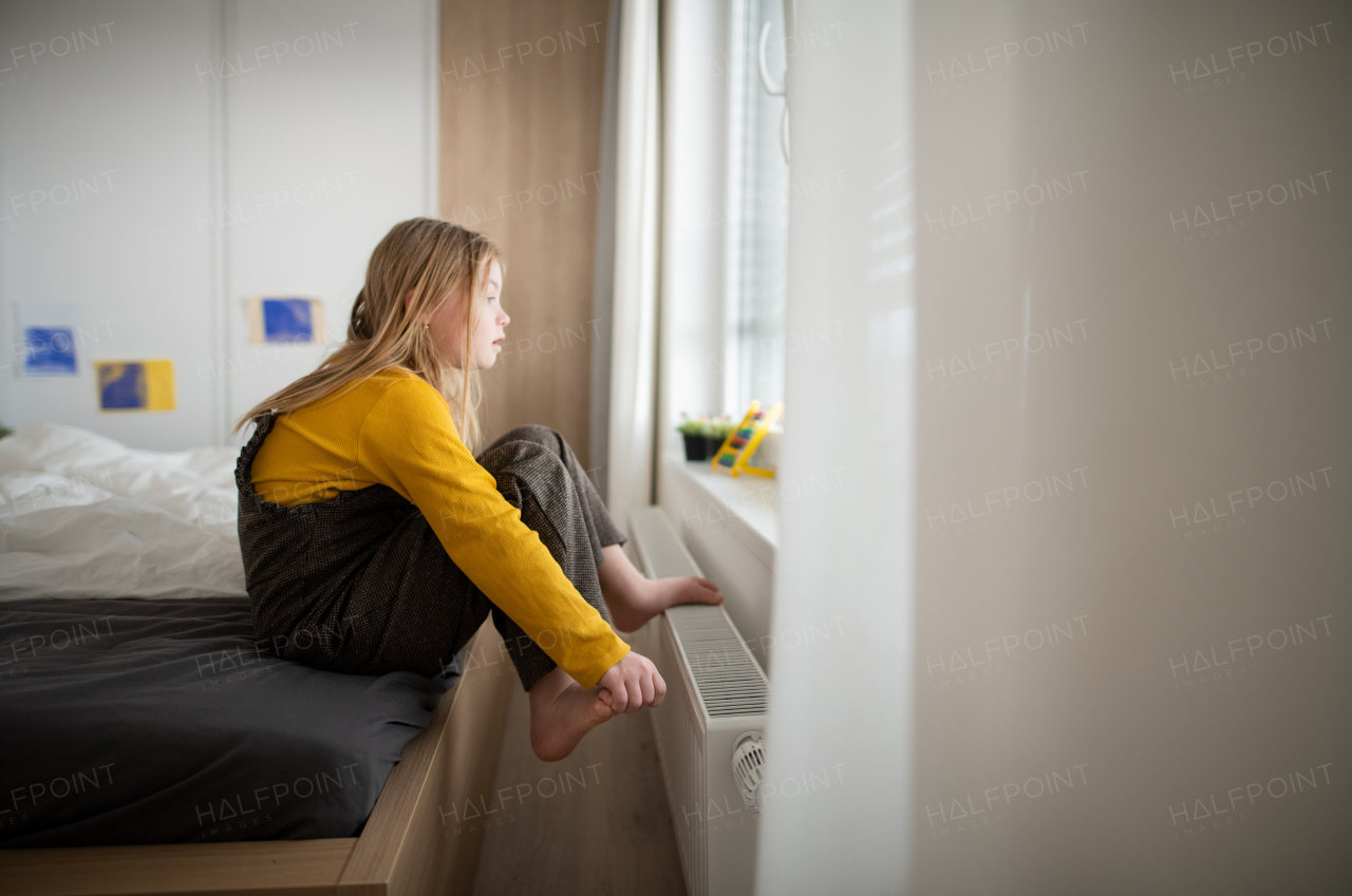 A curious little girl with Down syndrome looking through on window at home.