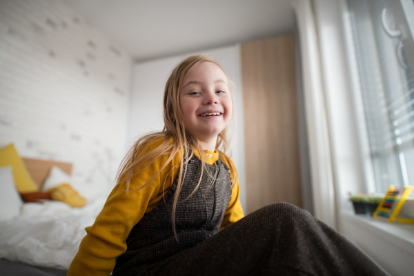 A happy little girl with Down syndrome sitting on bed at home.