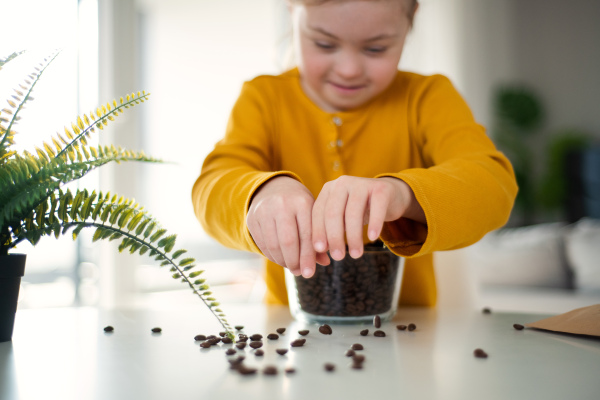 A little girl with Down syndrome sitting at table with bowl full of coffee beans at home.