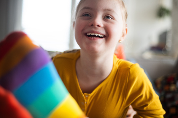 A close-up of cheerful little girl with Down syndrome lying on her father on bed.