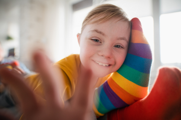 A close-up of cheerful little girl with Down syndrome lying on her father on bed and looking at camera.