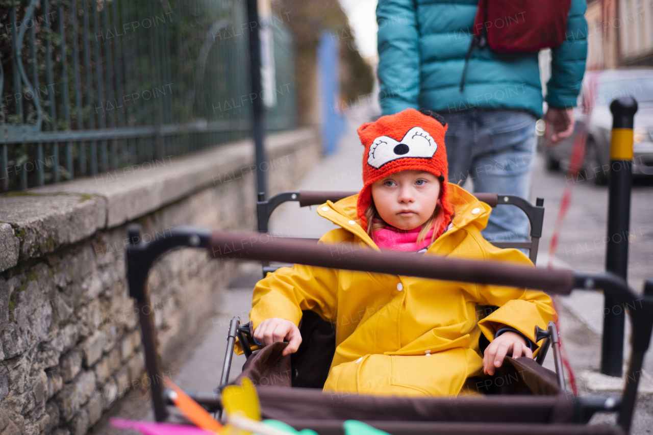 A father pulling his little daughter with Down syndrome in trolley on walk in town in winter.