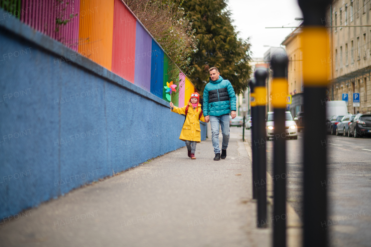 A father taking his little daughter with Down syndrome to school, outdoors in street.