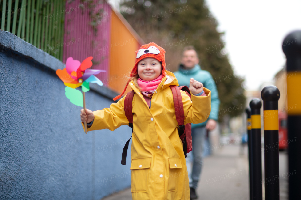 A father taking his little daughter with Down syndrome to school, outdoors in street.