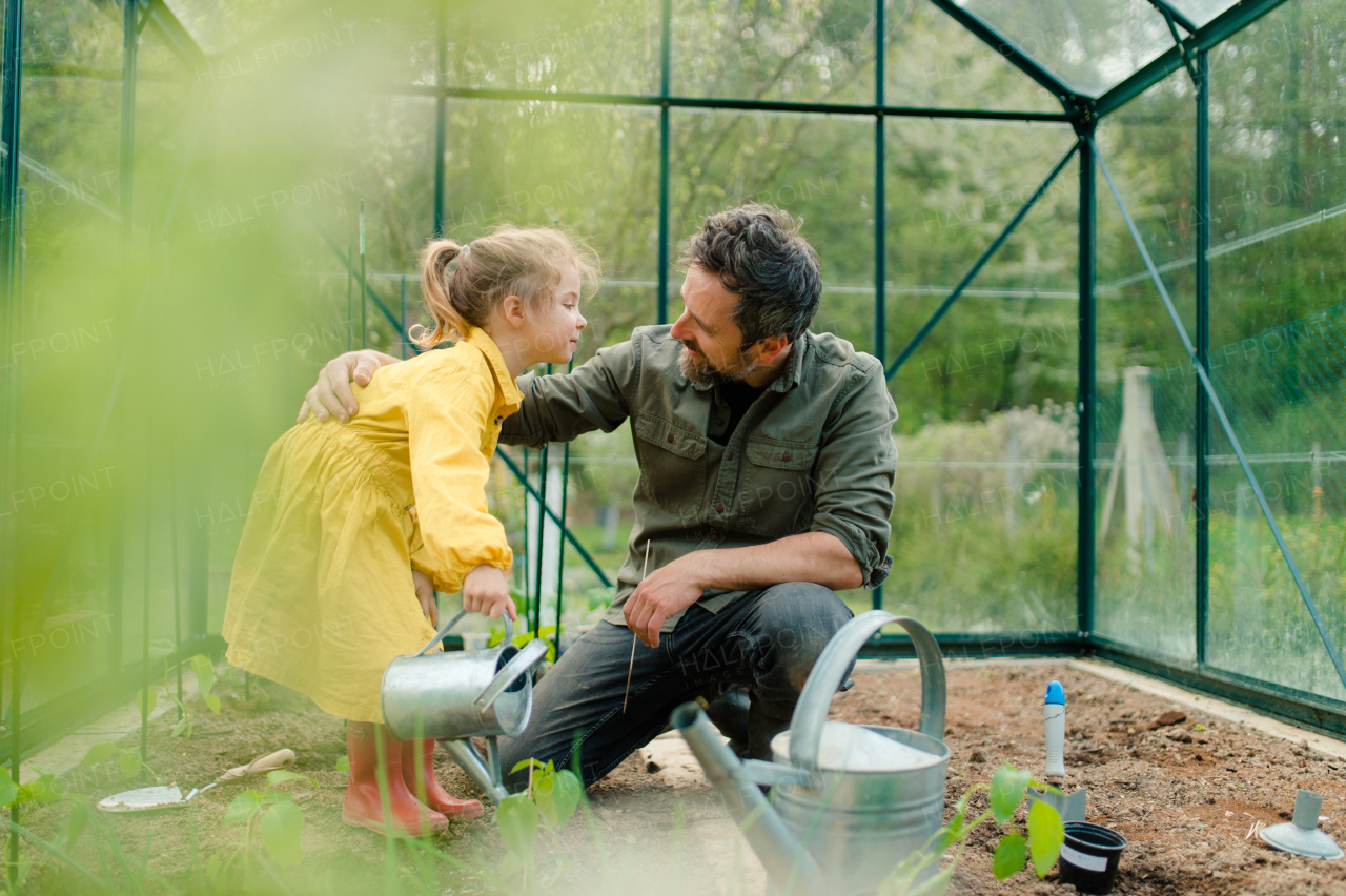 A father learning his little daughter to care about organic plants in eco greenhouse, sustainable lifestyle.