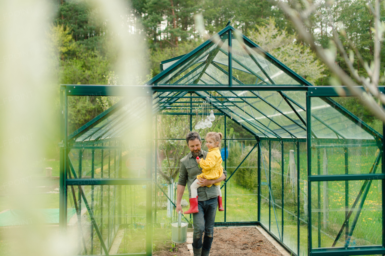 Father holding his little daughter in feco greenhouse,taking care of the vegetable together, sustainable lifestyle.