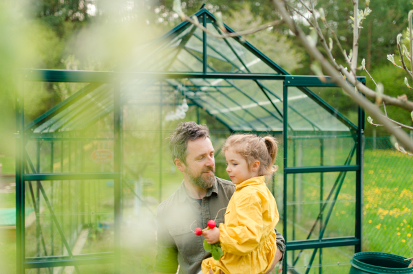 A father with his little daughter bonding in front of eco greenhouse, sustainable lifestyle.