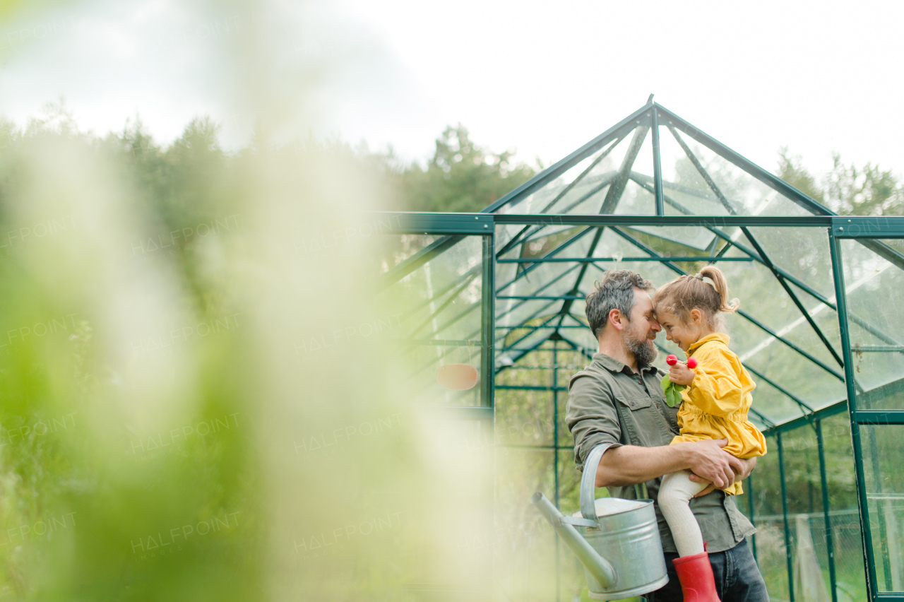 A gather with his little daughter bonding in front of eco greenhouse, sustainable lifestyle.