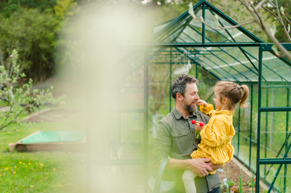 A gather with his little daughter bonding in front of eco greenhouse, sustainable lifestyle.