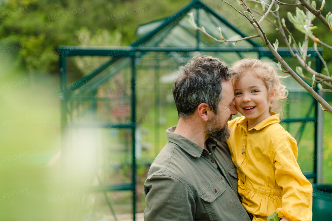 A father with his little daughter laughing in front of eco greenhouse, sustainable lifestyle.