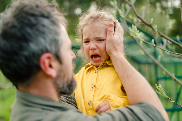 A father holding his crying little daughter and comforting her in garden