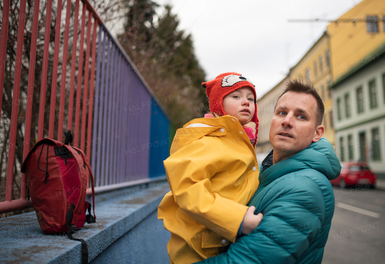 A father taking his little daughter with Down syndrome to school, outdoors in street.