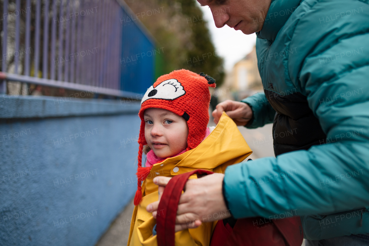 A father taking his little daughter with Down syndrome to school, outdoors in street.