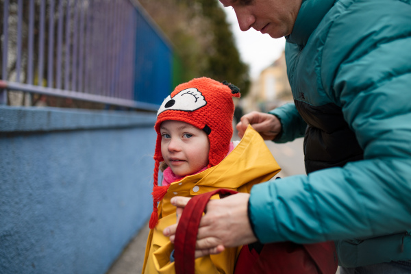 A father taking his little daughter with Down syndrome to school, outdoors in street.