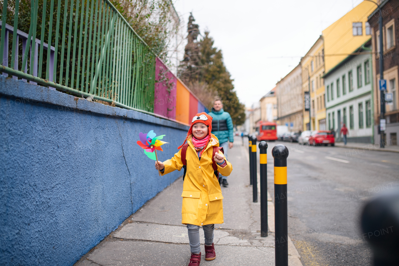 A father taking his little daughter with Down syndrome to school, outdoors in street.