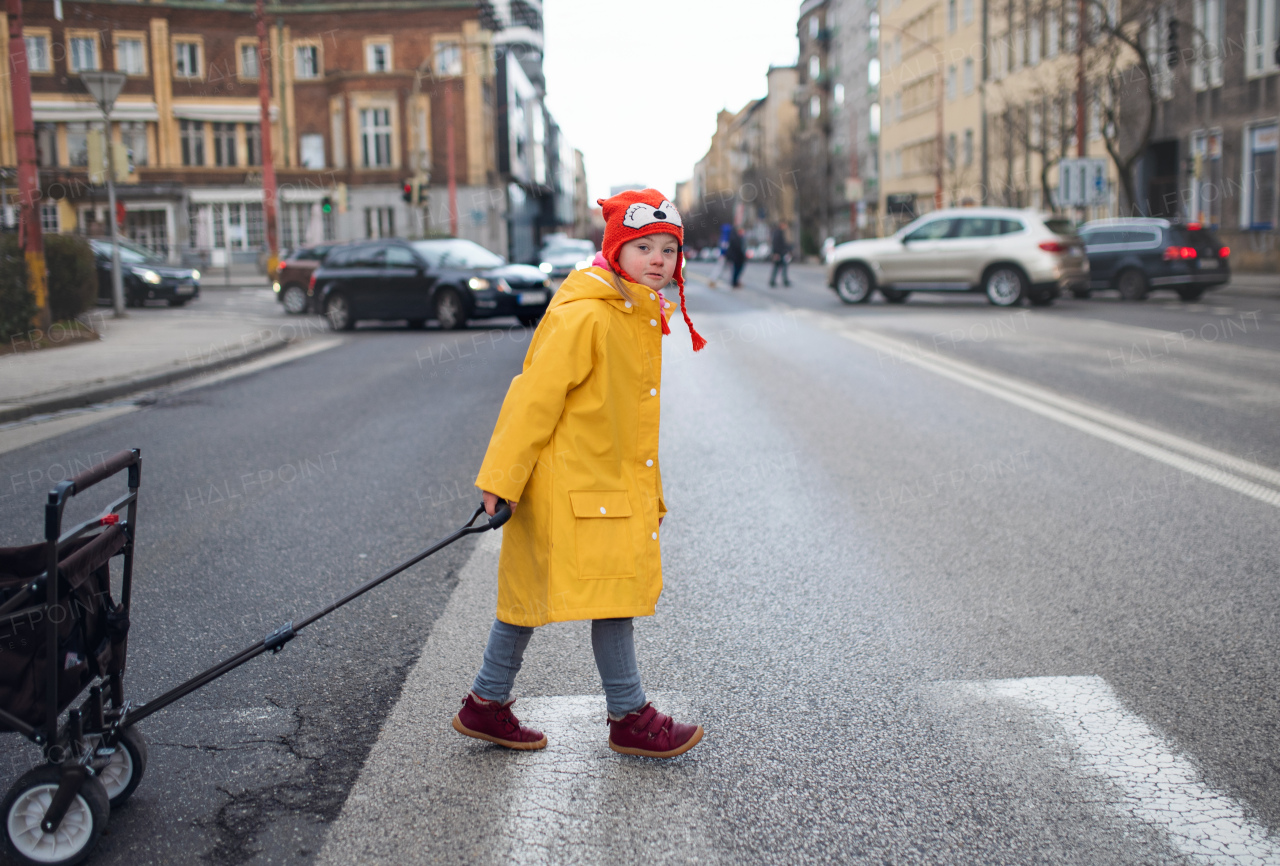 A little girl with Down syndrome crossing the road and pulling the trolley.