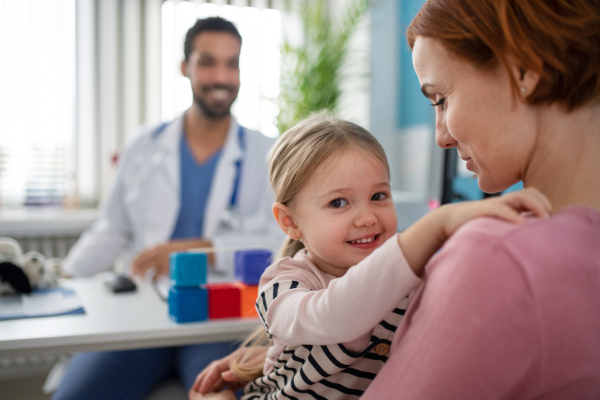 A little girl with her mother at doctor's office on consultation, looking at camera.