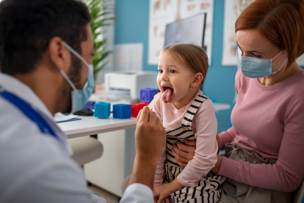 A zoung male doctor checking little girl's throat in his office.