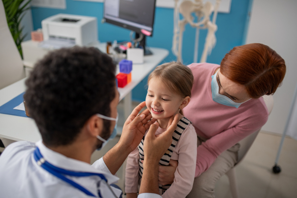 A young male doctor checking little girl's lymph nodes in his office.