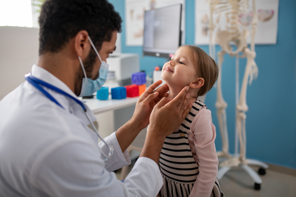 A young male doctor checking little girl's lymph nodes in his office.