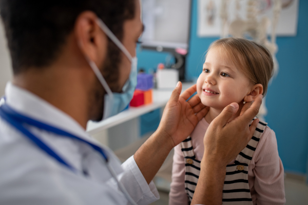 A young male doctor checking little girl's lymph nodes in his office.