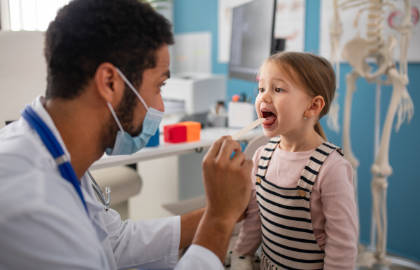 A zoung male doctor checking little girl's throat in his office.