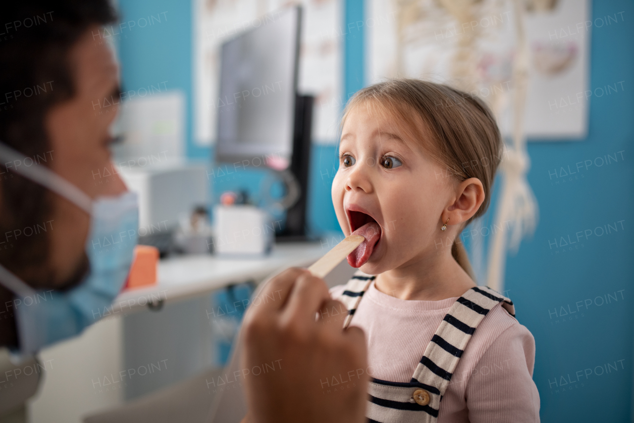 A zoung male doctor checking little girl's throat in his office.