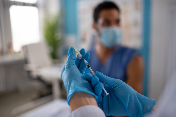 A close-up of doctor holding covid-19 vaccince syringe and preparing to give it to her colleague.