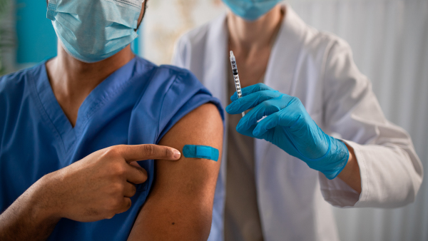 A close-up of unrecognizable doctor showing bandage on his arm after vaccince.