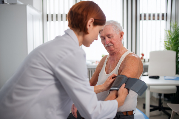 A female doctor measuring blood pressure to senior man patient in her office.