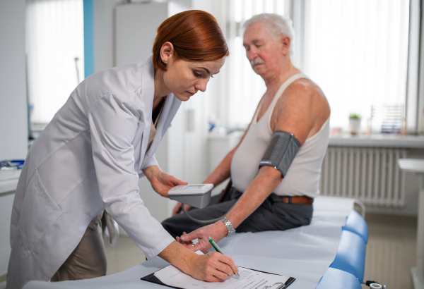 A female doctor measuring blood pressure to senior man patient in her office.