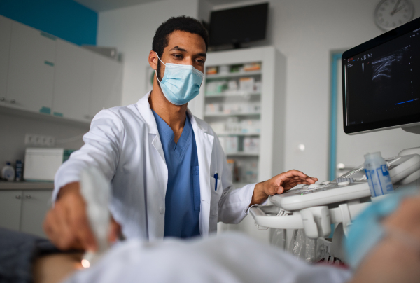 A young doctor is examining patient by using an ultrasound equipment in clinic, coronavirus concept.