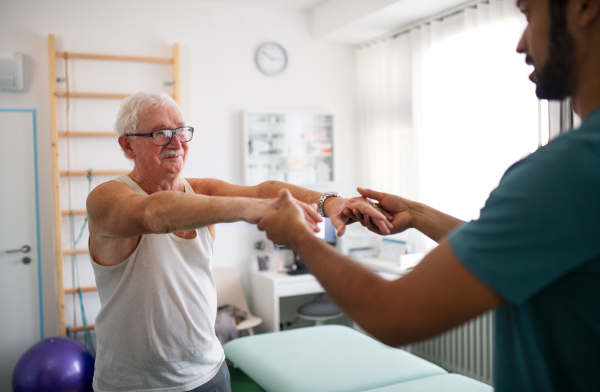 A young physiotherapist exercising with senior patient in a physic room.