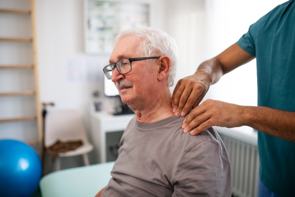 A young physiotherapist massaging the neck of senior patient in a physic room