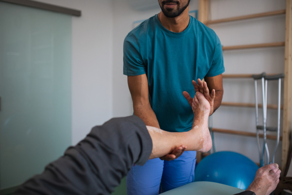 A close-up of physiotherapist exercising with senior patient's leg in a physic room.