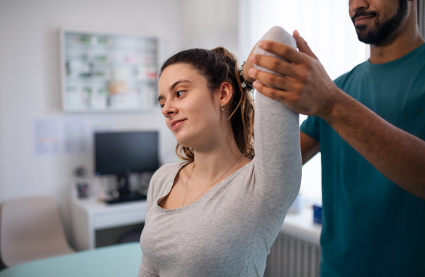 A young male physiotherapist examining young woman patient in a physic room