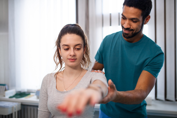 A young male physiotherapist examining young woman patient in a physic room