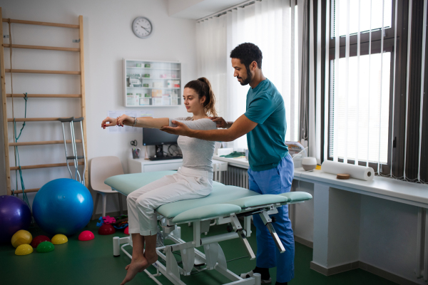 A young male physiotherapist examining young woman patient in a physic room