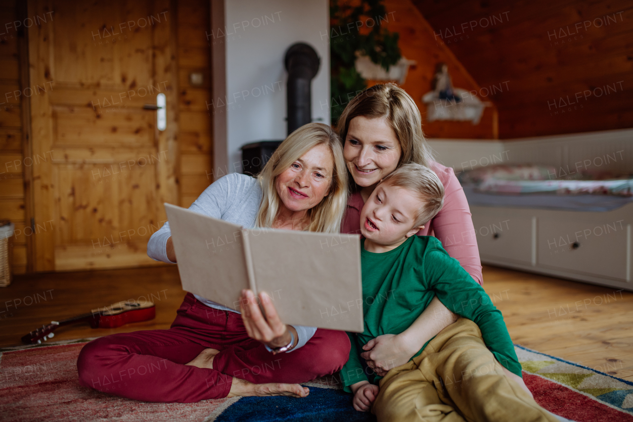 A boy with Down syndrome with his mother and grandmother looking at family photo album at home.